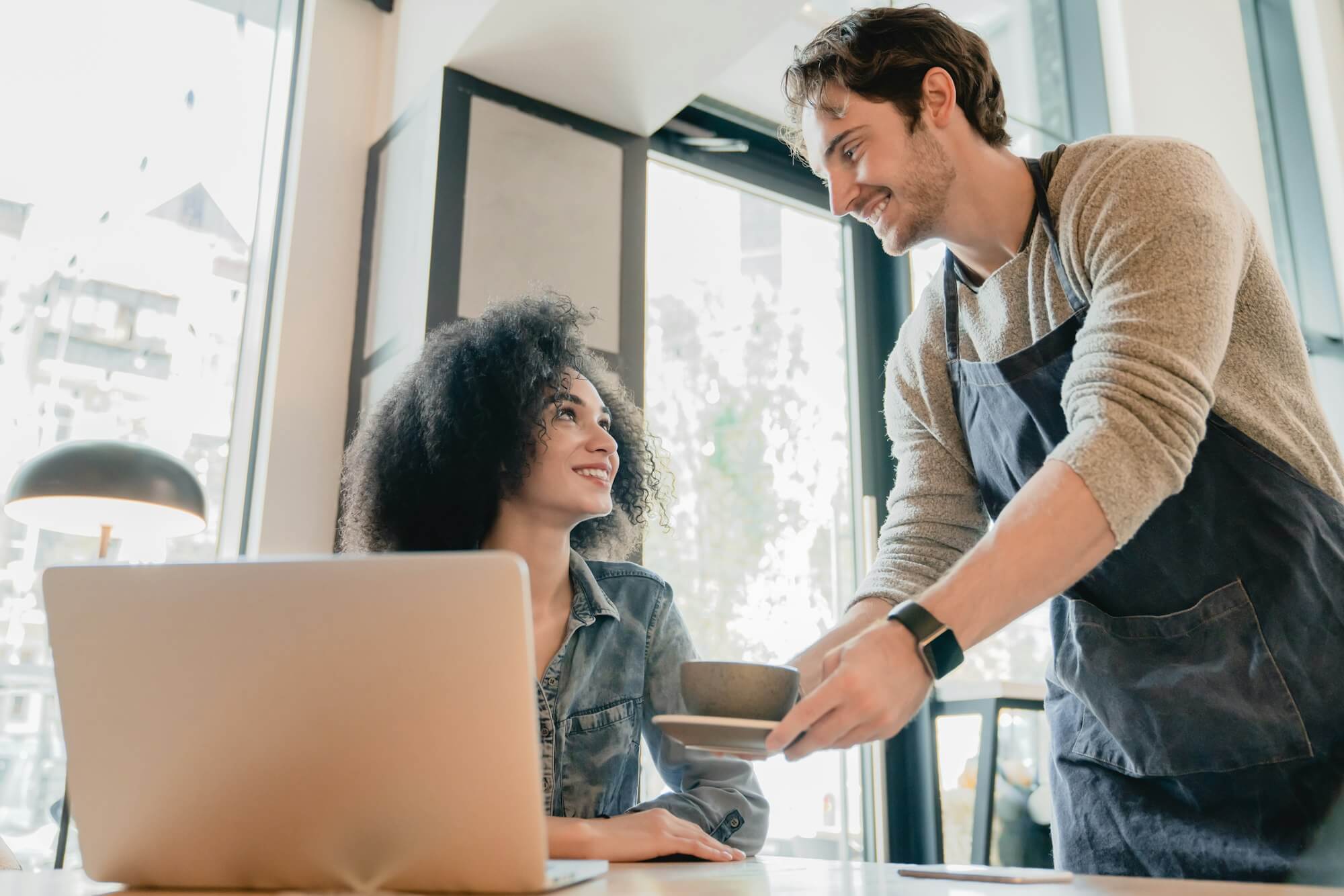 young-handsome-waiter-servicing-black-girl-customer-with-laptop-in-cafe.jpg